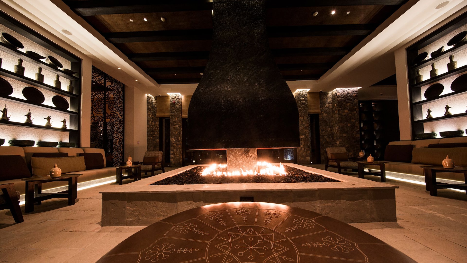 Lounge seating surrounding a central fire pit beneath a dark timber ceiling, Alila Jabal Akhdar, Jebel Akhdar, Oman