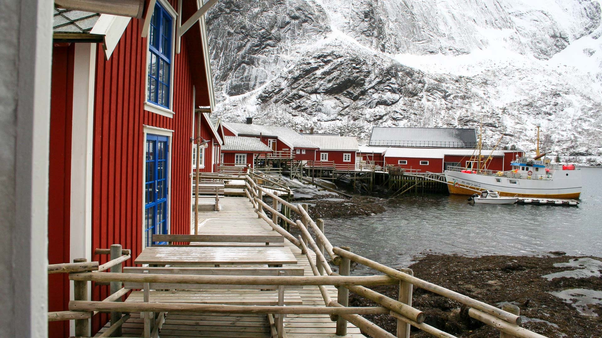 Waterfront cabin walkways beneath snowy mountains at Reine Rorbuer, Reine, Norway