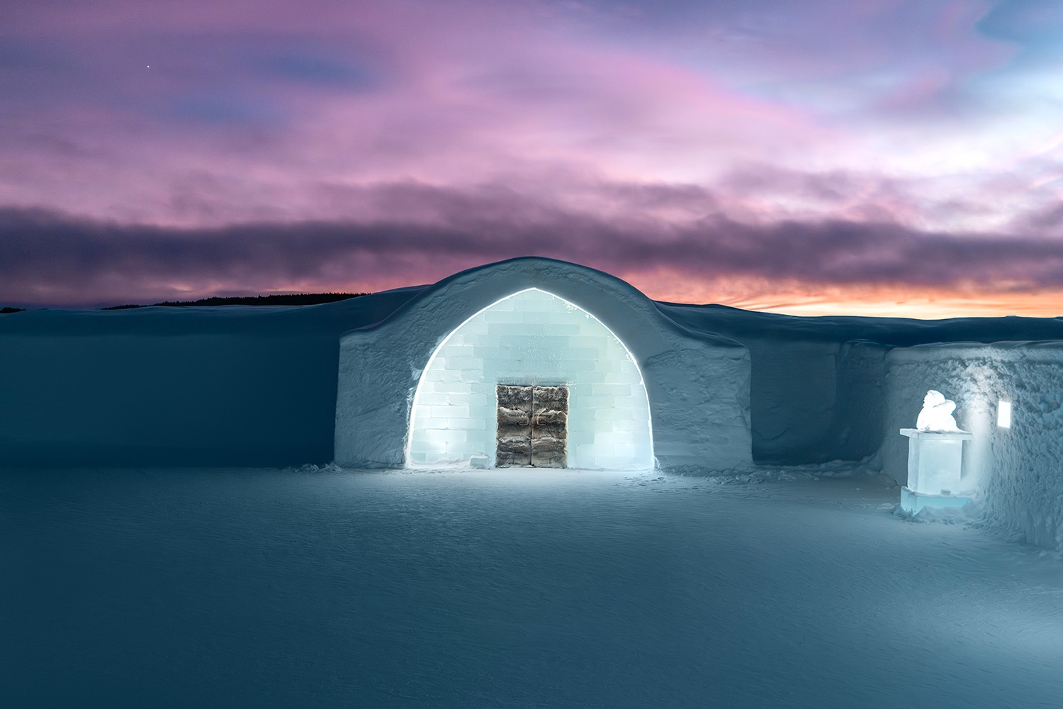Illuminated snow-and-ice entrance beneath a twilight sky at Icehotel, Jukkasjärvi, Swedish Lapland