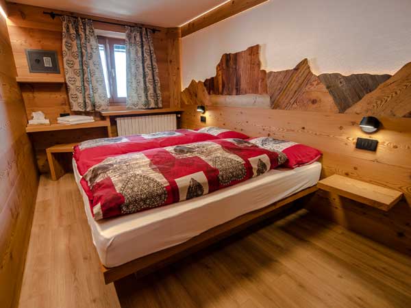 Wood-panelled double bedroom with red bedding and a mountain-shaped headboard at Rifugio Lagazuoi, Dolomites, Italy