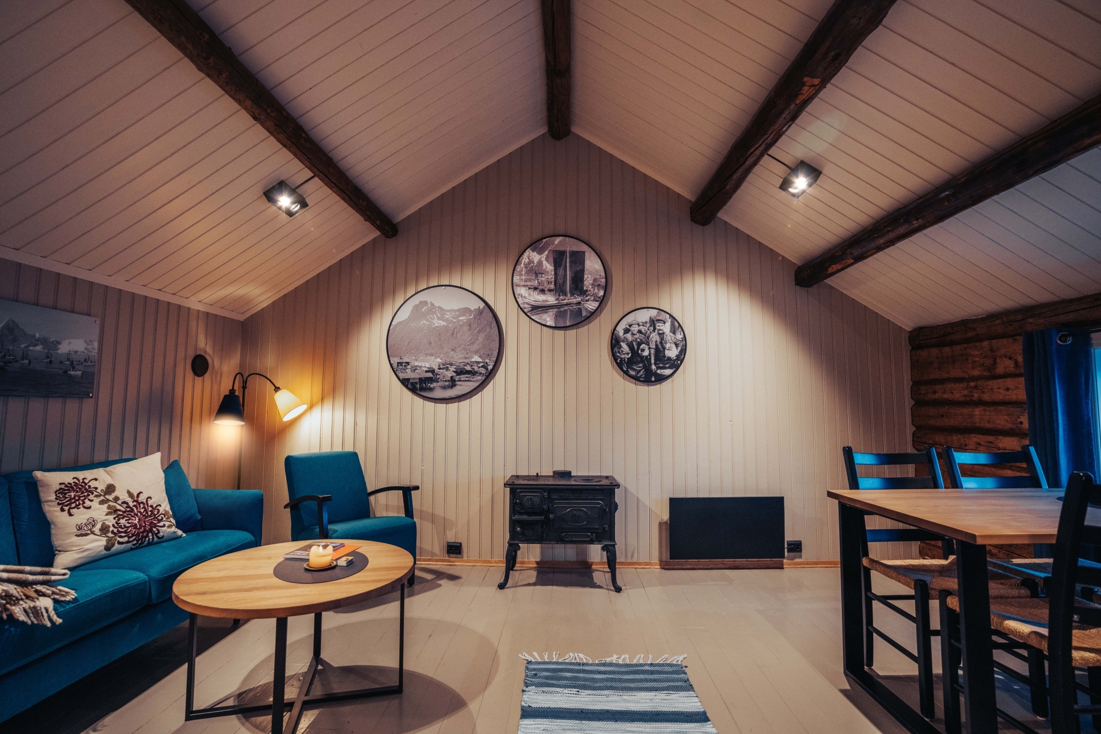 Cabin living area with blue sofa, round tables, timber ceiling and dining counter at Svinøya Rorbuer, Lofoten, Norway