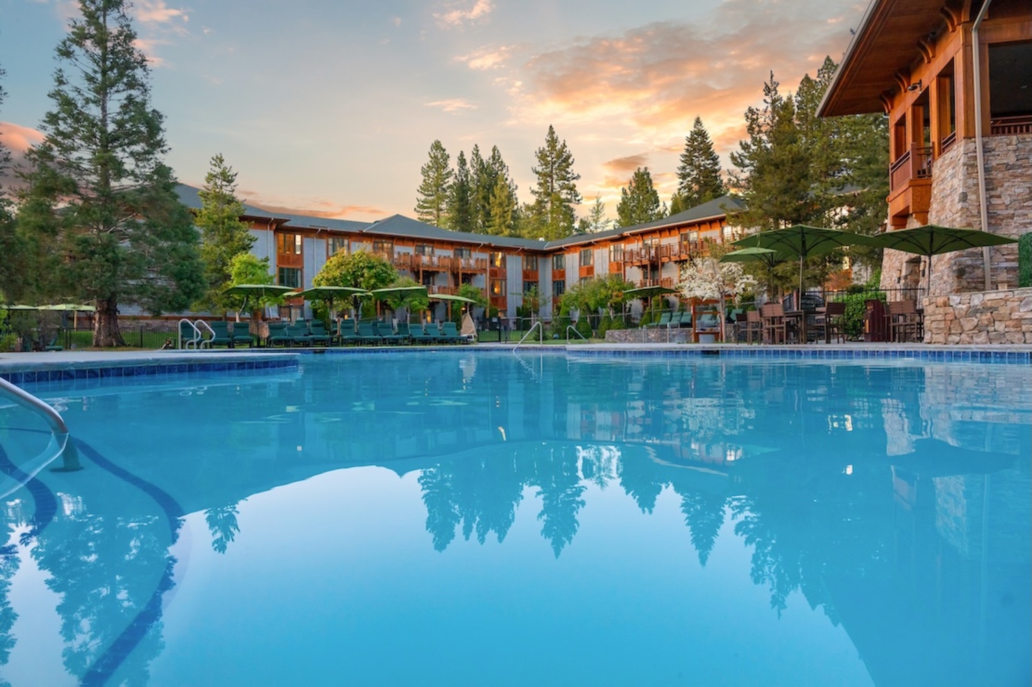 Outdoor swimming pool at twilight surrounded by resort buildings and pine trees at Hyatt Regency Lake Tahoe