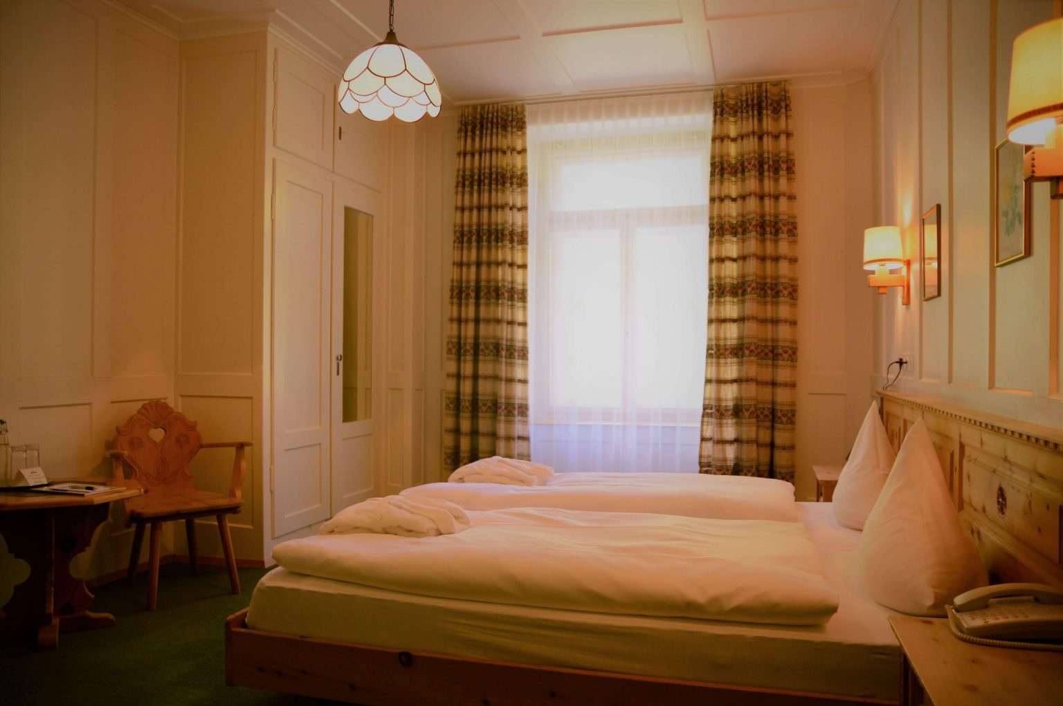 Pine-panelled bedroom with twin bedding, curtains and a pendant lamp at Berghotel Schatzalp, Davos, Switzerland
