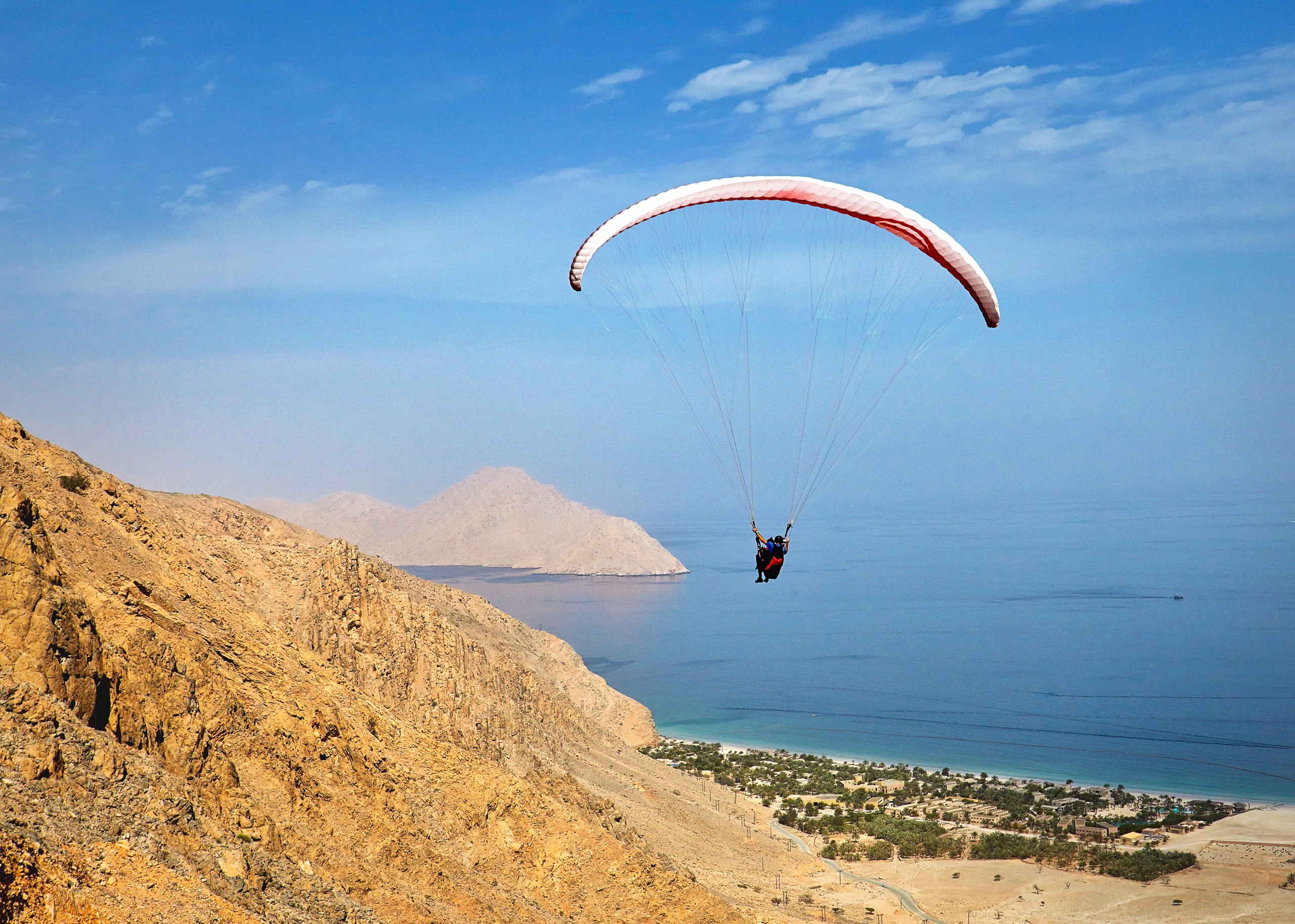 Tandem paraglider above the rocky mountainside overlooking Zighy Bay and the sea, Six Senses Zighy Bay