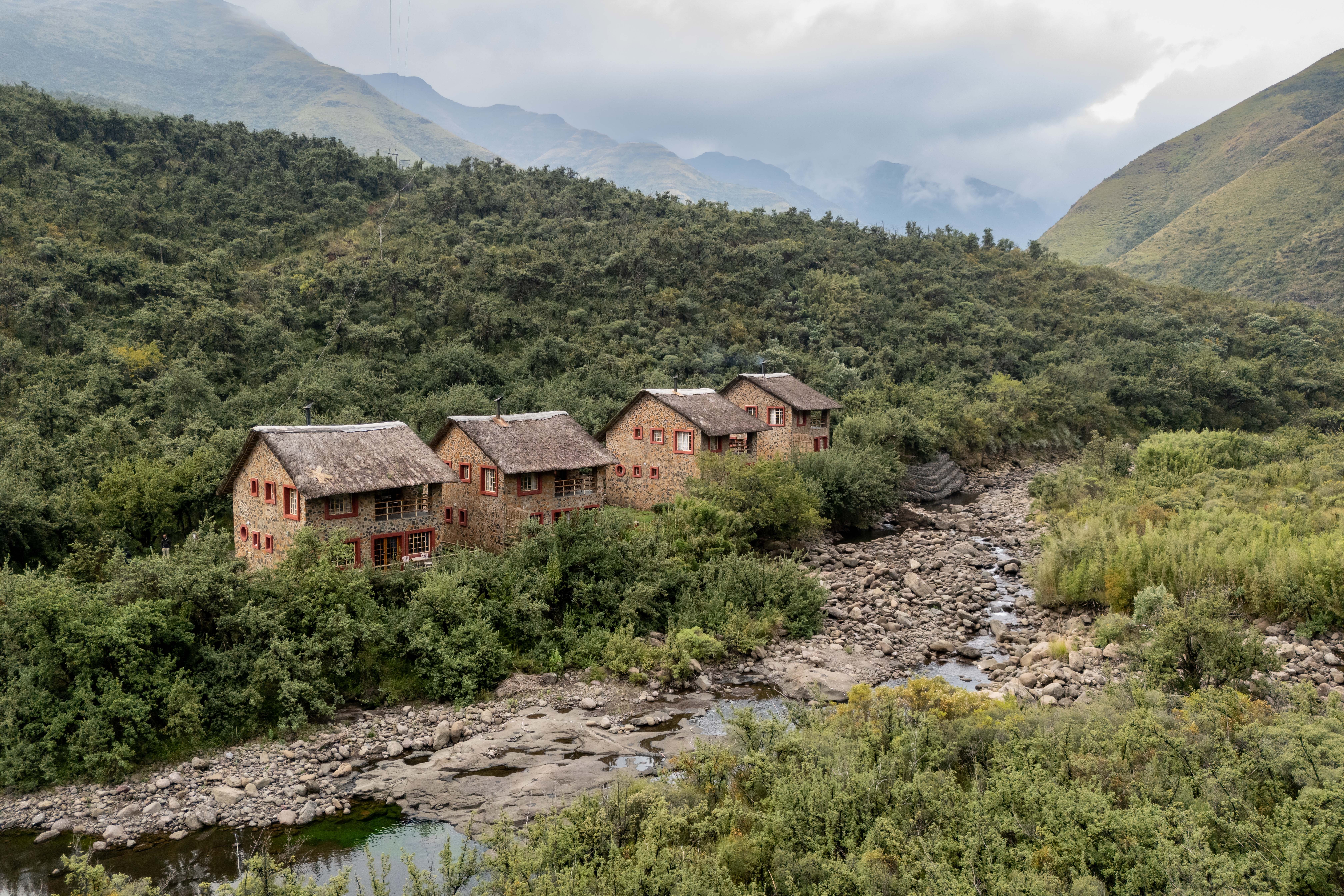 Riverside lodge buildings surrounded by forested mountains, Maliba Mountain Lodge, Ts’ehlanyane National Park, Lesotho
