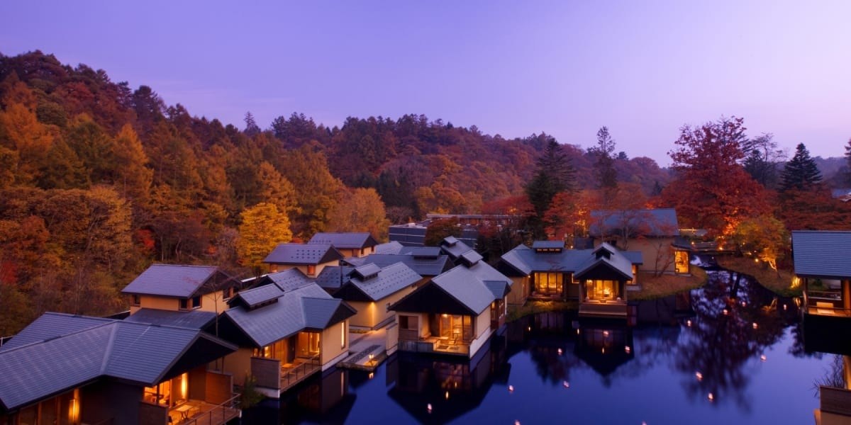 Waterside pavilions glowing at dusk beneath a hillside of autumn foliage, Hoshinoya Karuizawa