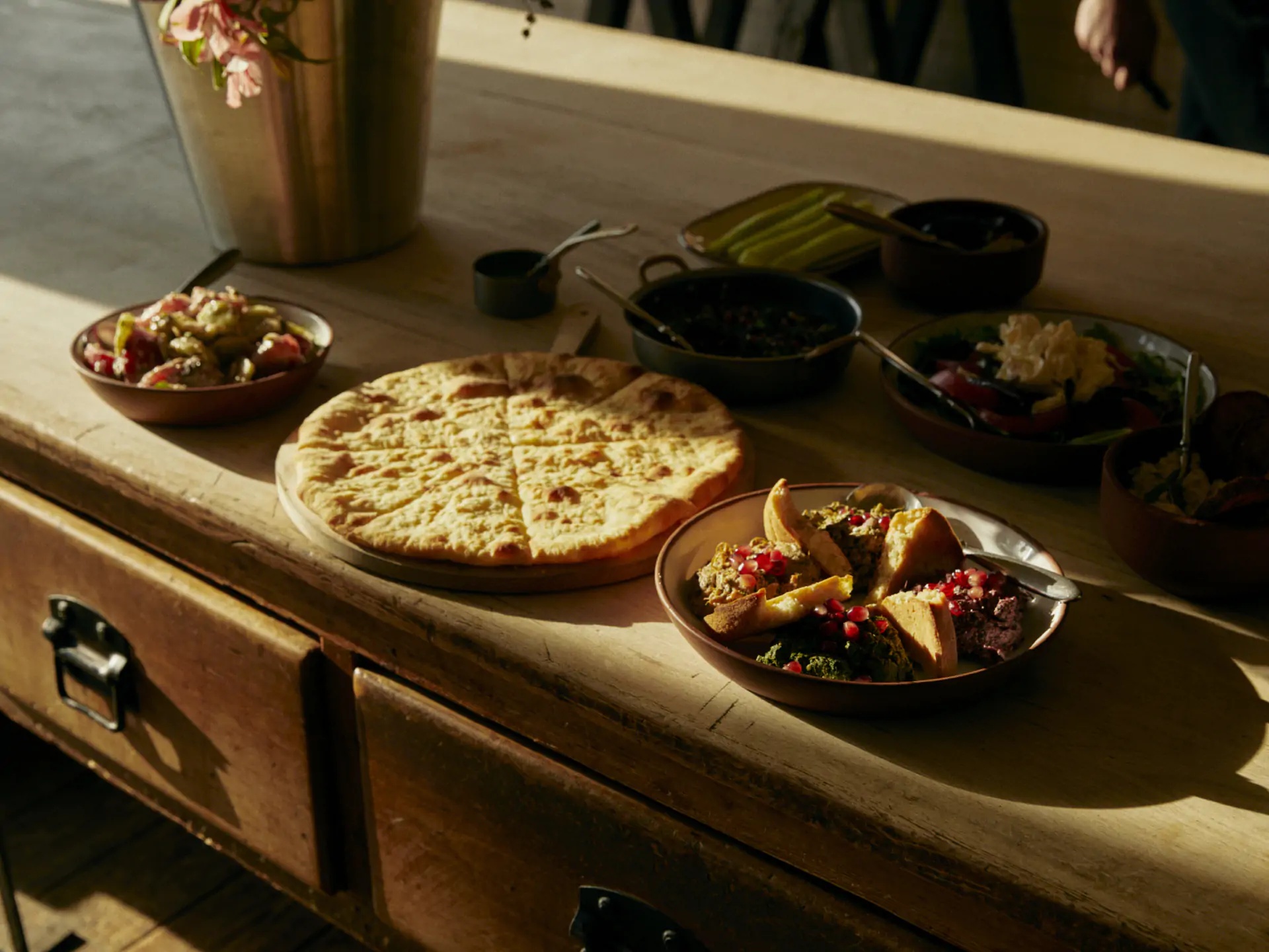 Round flatbread and vegetable dishes on a wooden restaurant counter at Rooms Hotel Kazbegi, Georgia