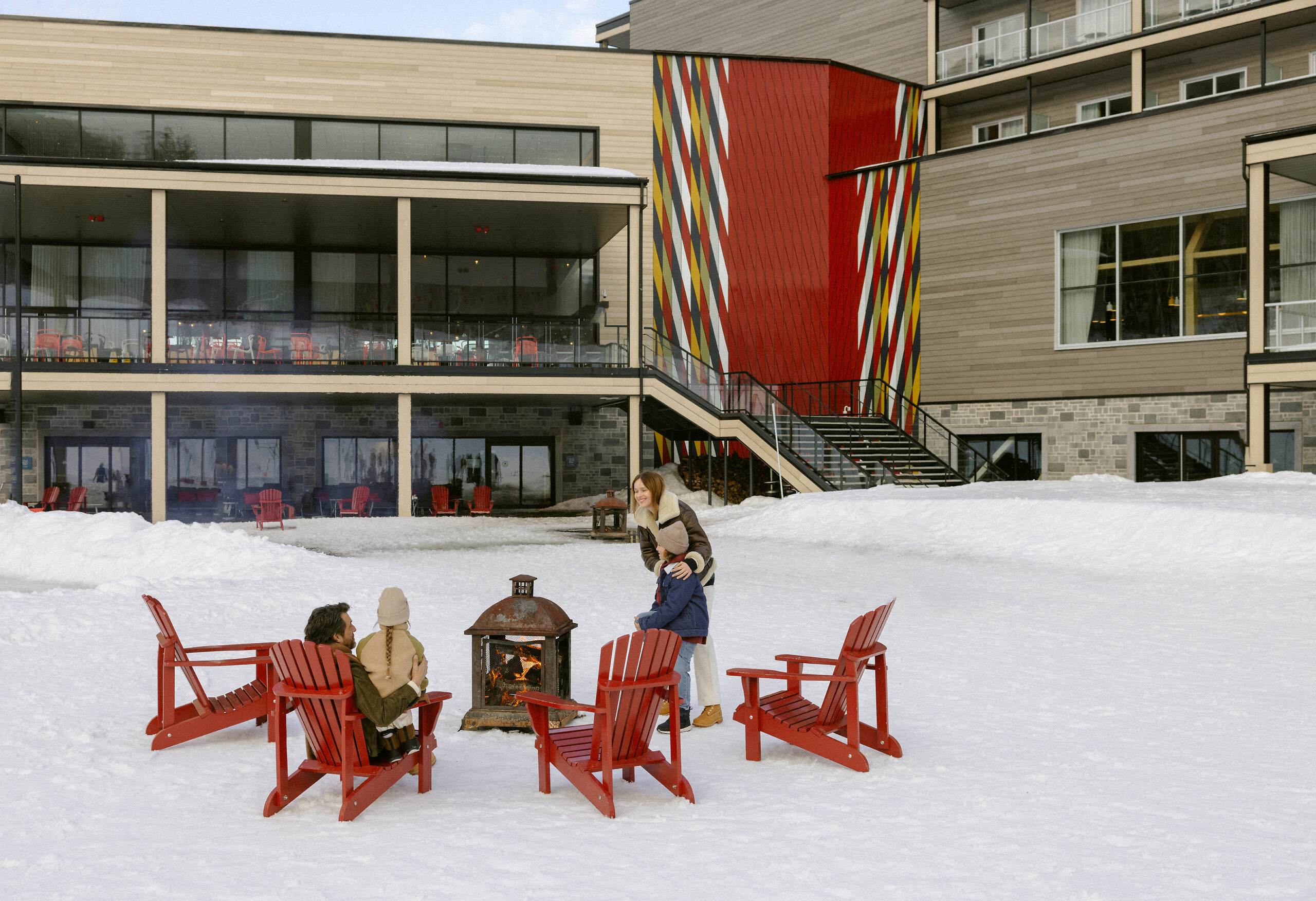 Snow-covered courtyard, red Adirondack chairs and timber-clad winter exterior at Club Med Québec Charlevoix