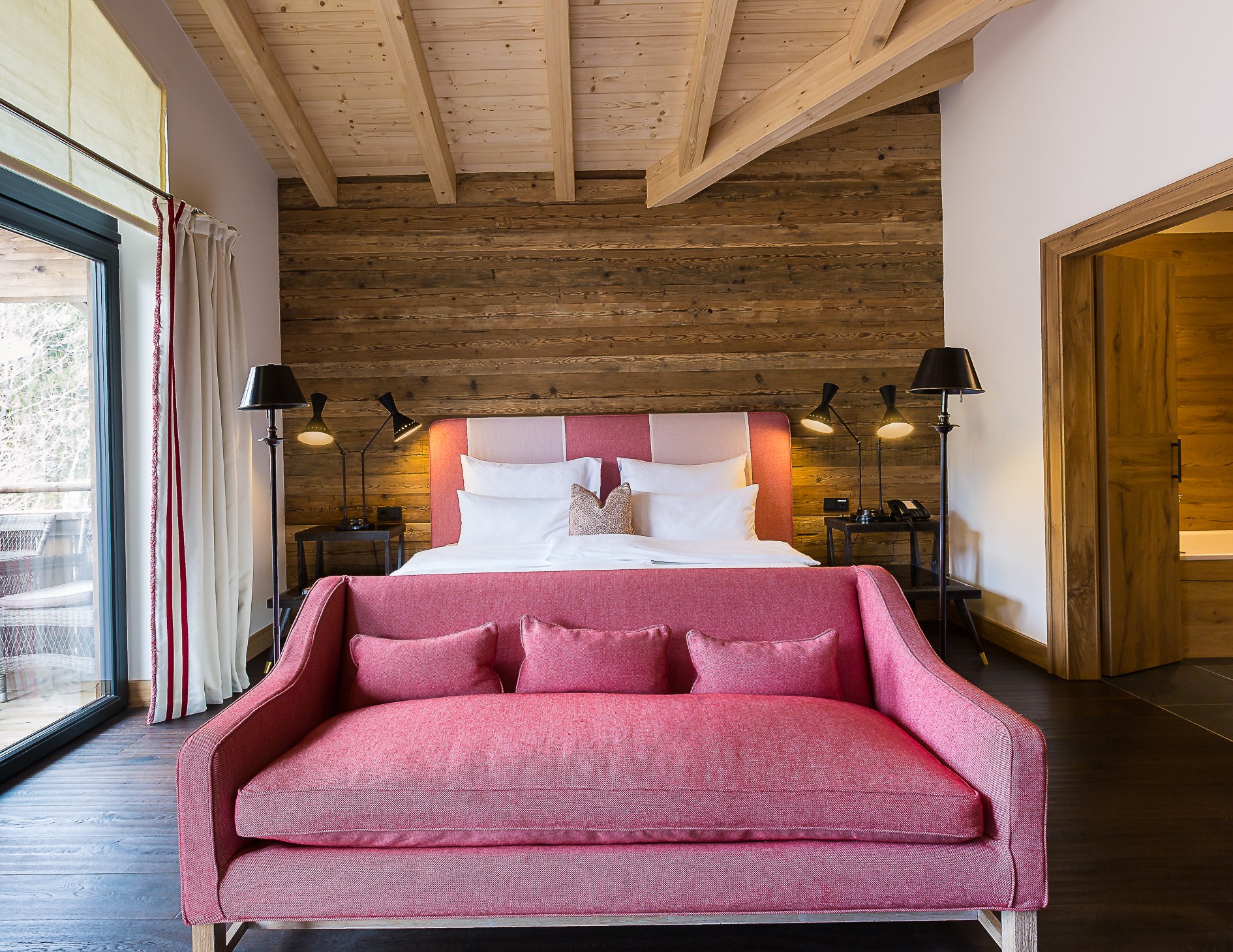 Timber-lined Alpine guest room with pink upholstered bed and seating at House of Hütter – Wachtelhof