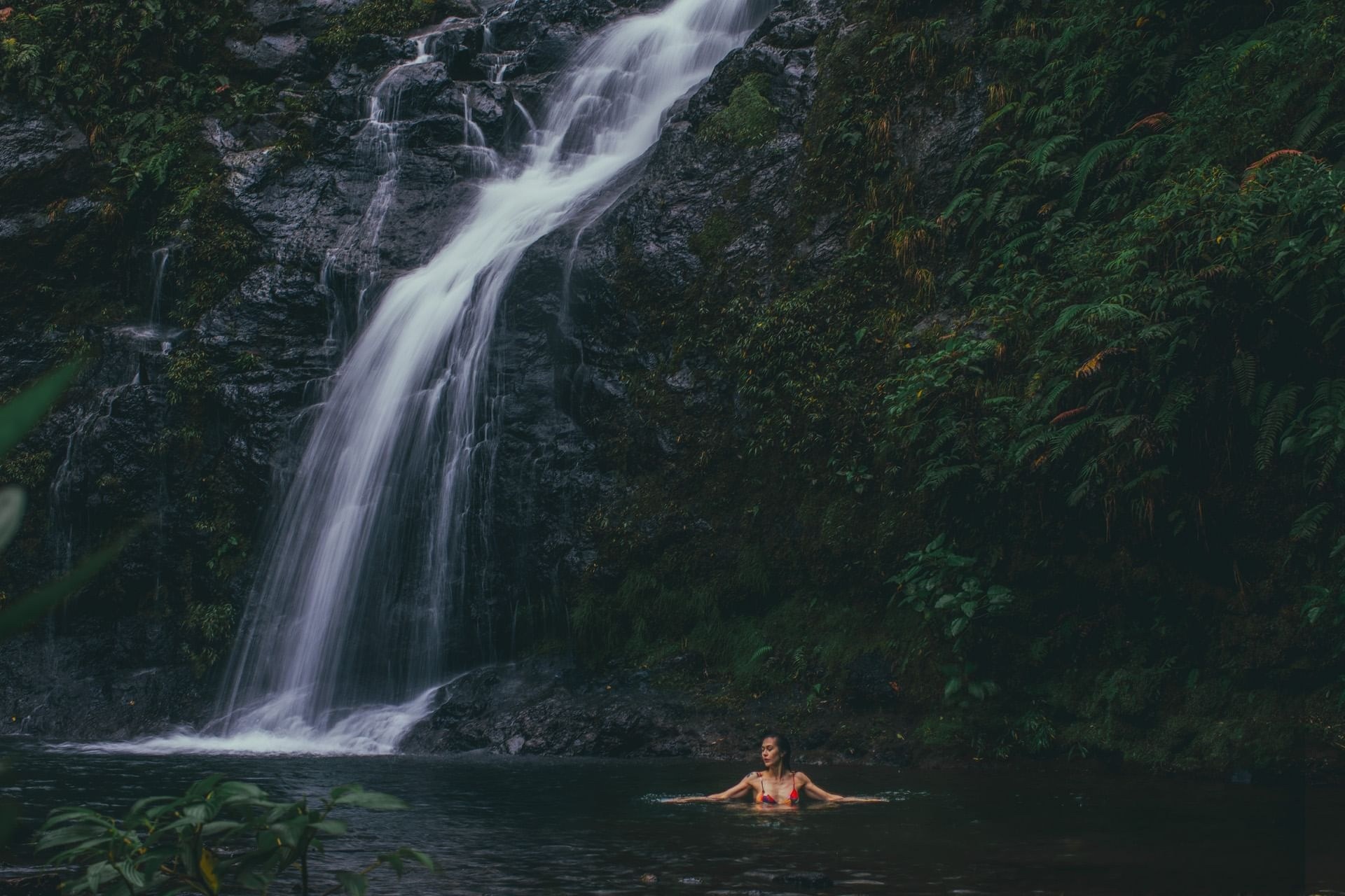 Waterfall cascading into a forest pool with a swimmer in the water, El Silencio Lodge & Spa