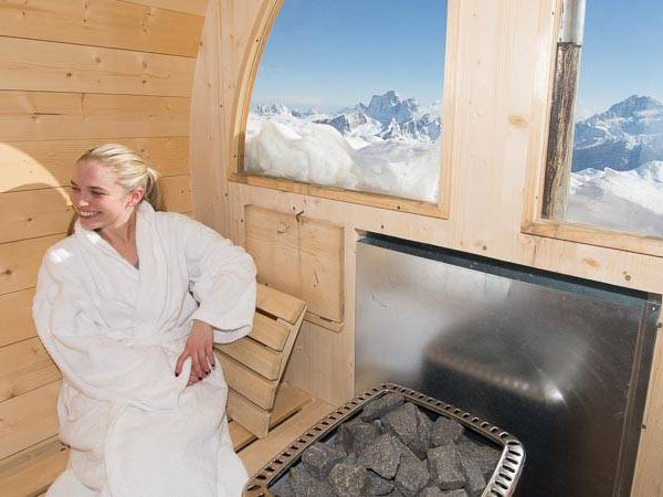 Guest in a bathrobe in the wooden sauna with a mountain-facing window at Rifugio Lagazuoi, Dolomites