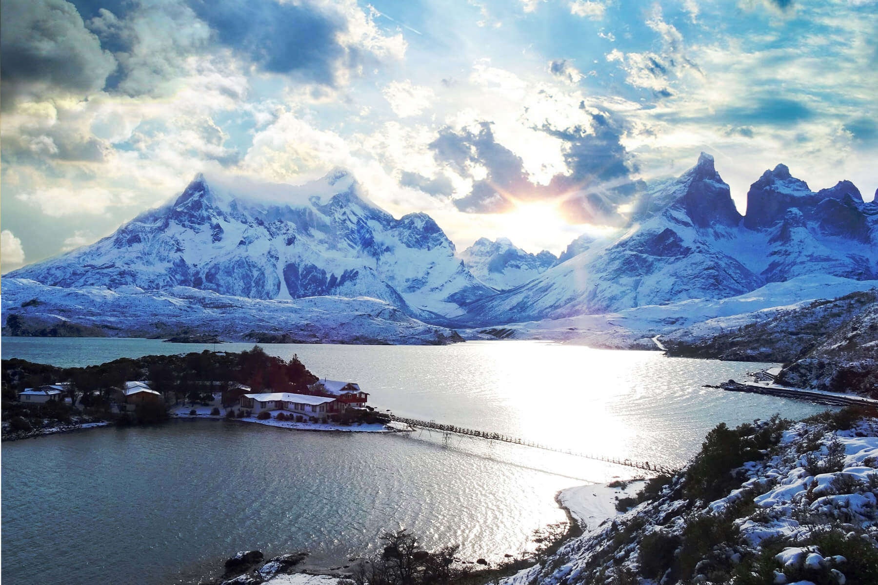 Island lodge and pedestrian bridge across Lake Pehoé beneath snowy mountains, Torres del Paine, Chile
