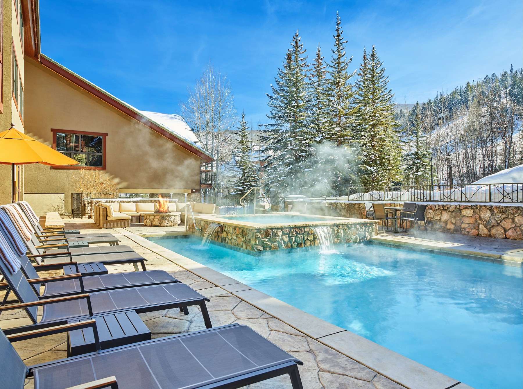 Poolside sun loungers beside the steaming hot tub at The Osprey at Beaver Creek, with ski slopes beyond.
