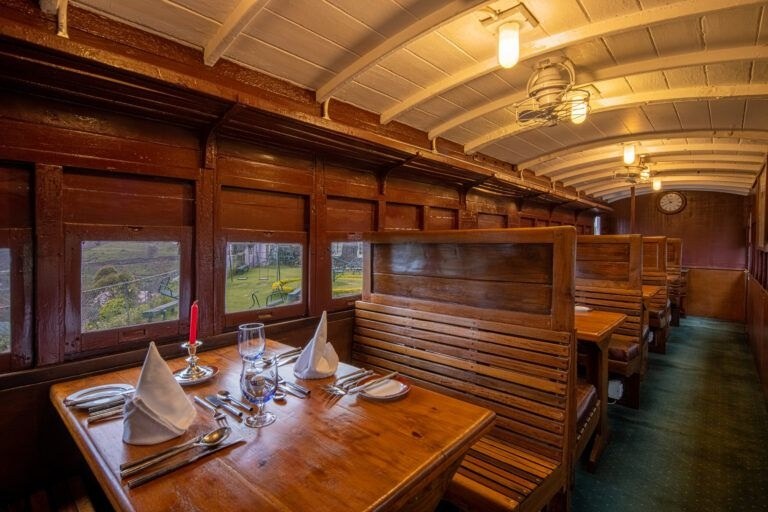 Wood-panelled railway carriage restaurant with a table set for dining, Heritance Tea Factory