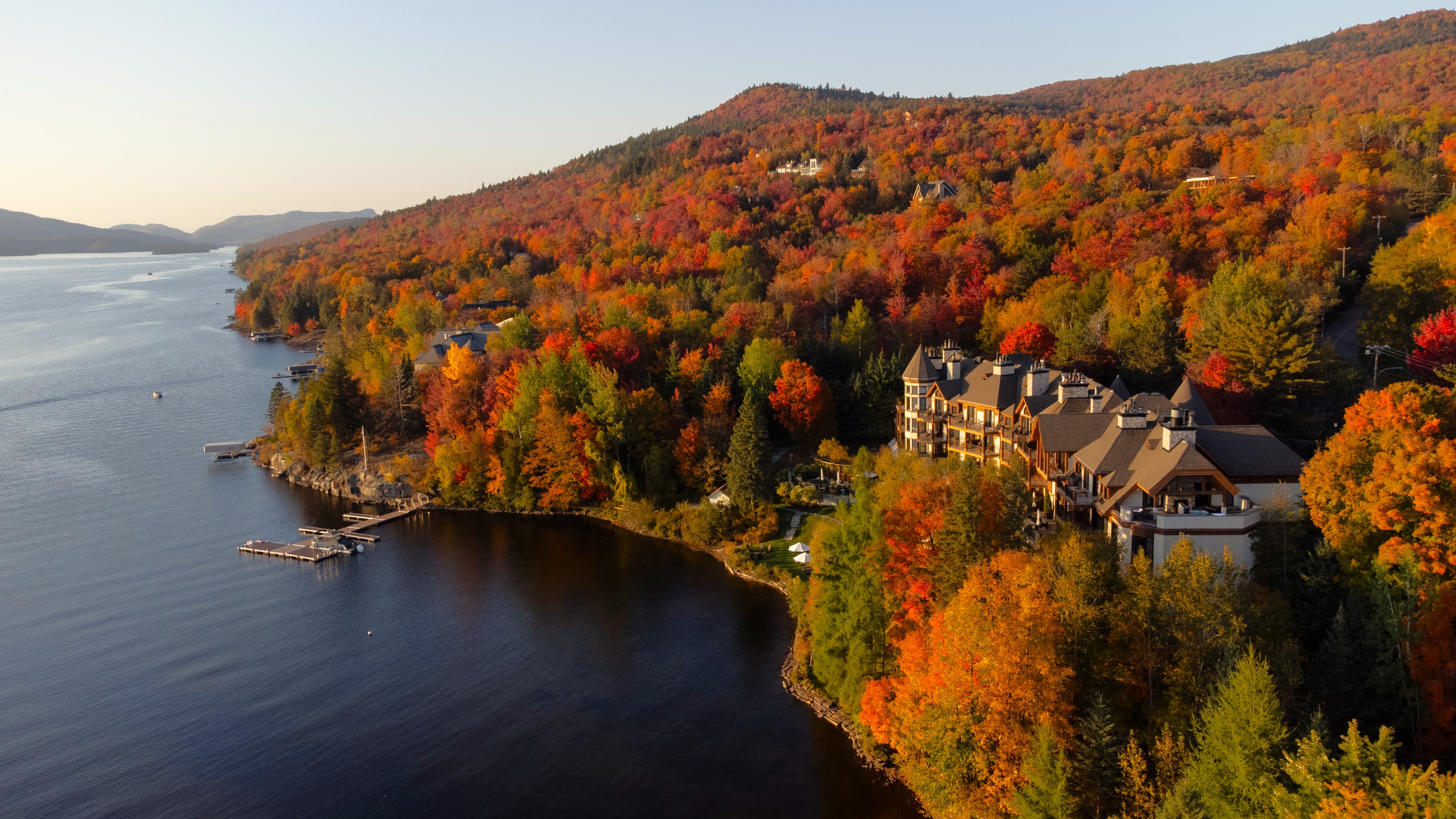 Aerial view along Lake Tremblant showing blue water, autumn woodland and the hotel on the shoreline at Hôtel Quintessence