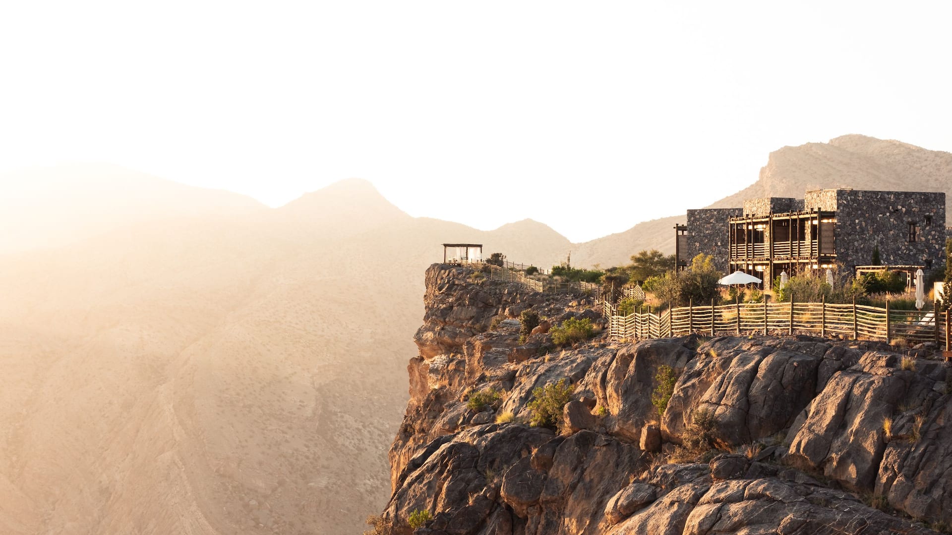 Stone resort buildings perched on a sunlit canyon rim with mountains beyond, Alila Jabal Akhdar, Jebel Akhdar, Oman