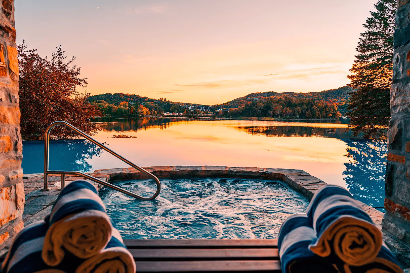 Bubbling outdoor spa hot tub with metal handrails and rolled towels, overlooking Lake Tremblant at sunset at Hôtel Quintessence