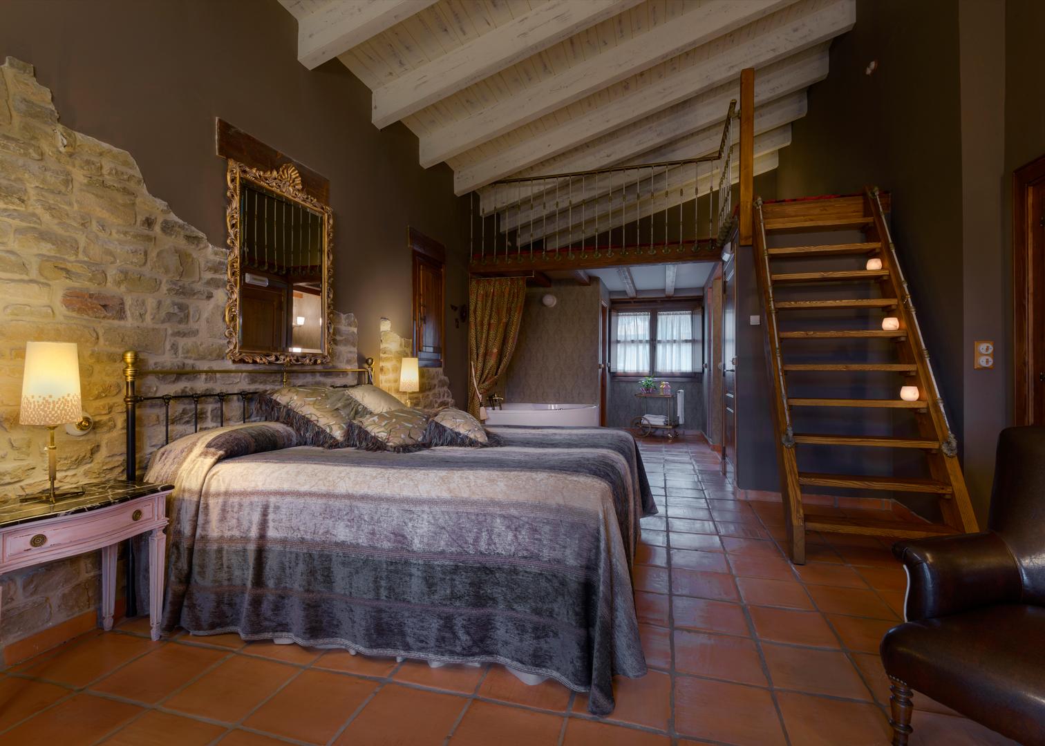 Guest room with a wooden ceiling, exposed stone and stairs to a loft at Hotel Barosse, Jaca, Spain